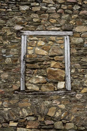 This rustic wall features a stone layout with various textures, framed by an aged wooden window. The materials reflect the character of rural architecture, revealing nature's touch through time. France