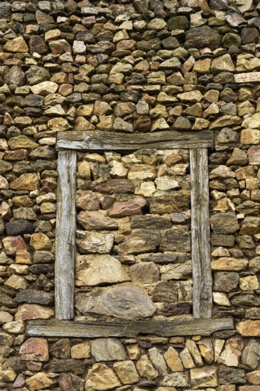 A wall constructed of unevenly arranged stones features a striking wooden frame that outlines an empty space where a window once existed, reflecting natural craftsmanship. France