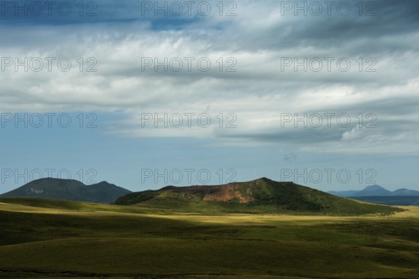 Mountains stretch across the landscape under a vast sky filled with dynamic clouds. Sancy Massif in Auvergne volcanoes Regional Natural Park. France