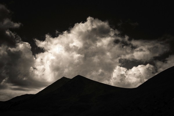 Majestic mountains form a dark outline against a backdrop of swirling clouds illuminated by twilight. Sancy Massif in Auvergne, France