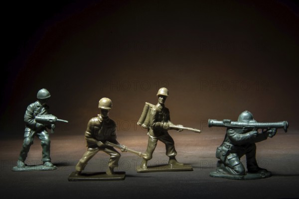 Four miniature soldier figures positioned in a tense standoff, showcasing various combat stances illuminated by a soft, dramatic light against a dark background