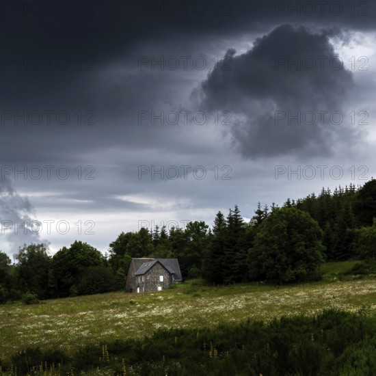 A solitary house stands in a lush green field under a sky filled with dark, ominous clouds. Auvergne. France