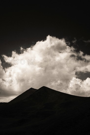 Majestic mountains form a dark outline against a backdrop of swirling clouds illuminated by twilight. Sancy Massif in Auvergne, France