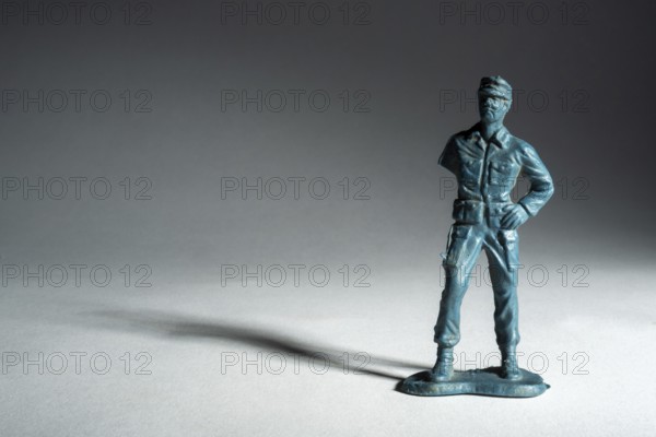 A small toy soldier figure stands upright with a confident pose. The soft lighting creates a dramatic interplay of shadows, enhancing the figure's vintage appeal