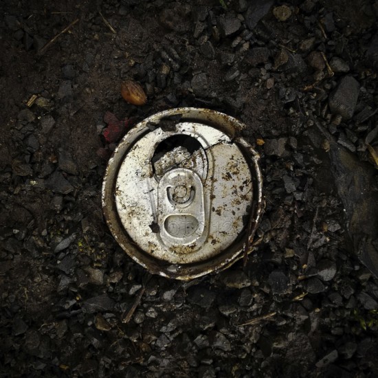 An aluminum can lies abandoned on dark, rich soil interspersed with small pebbles, underscoring the litter issue in outdoor environments under daylight