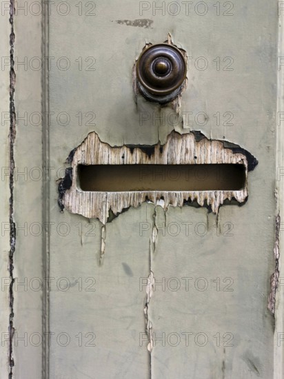 A weathered door in an urban setting features peeling paint and a rusty mail slot. The worn appearance reflects the passage of time and stories held within the city environment