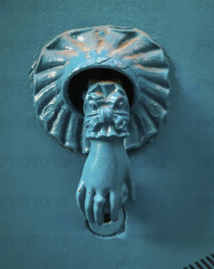 This unique door knocker features a lion's paw design with detailed craftsmanship. Its turquoise color contrasts wonderfully with the blue background, promising an inviting entrance
