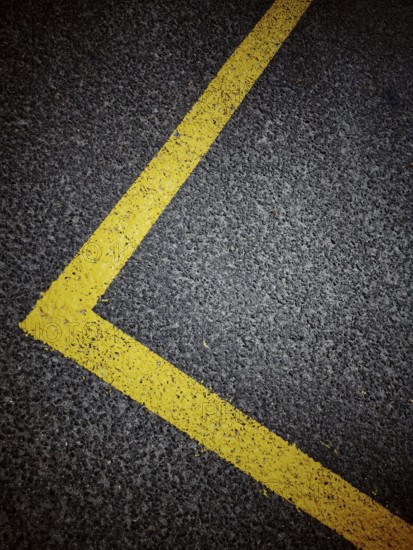 Bright yellow line marking outlines the dimensions of a parking space on a dark asphalt surface in an urban setting, highlighting organized space usage and road management