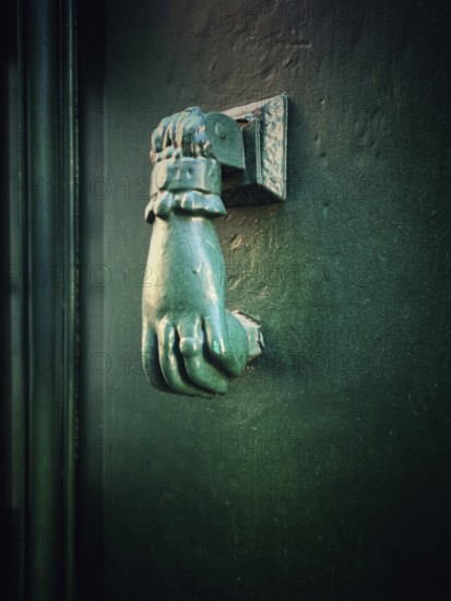 A distinctive bronze hand-shaped door knocker is mounted on a teal door, reflecting intricate craftsmanship while complementing the historic architecture of the building