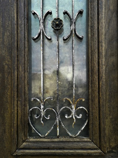 Craftsmanship shines through this wooden door, featuring beautiful metal designs and colorful glass panels. It adds charm to a rustic village setting, blending artistry and nature