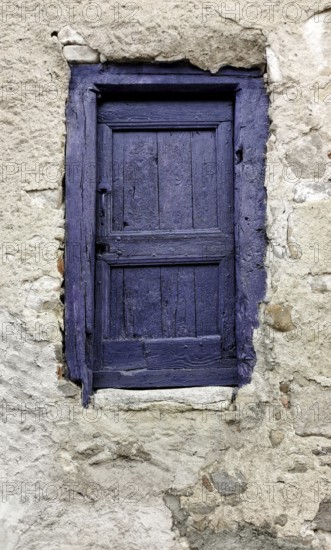 A small door painted in vibrant purple contrasts beautifully with a weathered stone wall. The rustic charm adds character and visual interest to the quaint backdrop