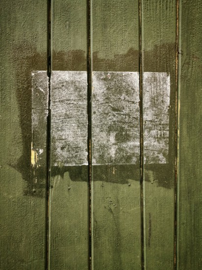 A rectangular patch on a green wooden surface shows faded remnants of a past application, with chipped paint revealing the wood grain. The area indicates age and neglect
