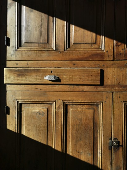A vintage wooden cabinet features a prominent drawer, bathed in warm sunlight that casts shadows. The rustic design highlights the texture and craftsmanship of the wood