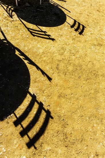 Shadows cast by chairs and tables stretch across a sunlit ground, revealing intricate patterns on the warm surface. This captivating scene evokes a sense of tranquility and leisure