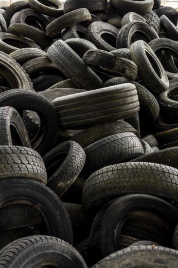 A large collection of worn tires is heaped together in a cluttered industrial setting. The scene captures the texture and patterns of the tire surfaces, showcasing their weathered condition. France