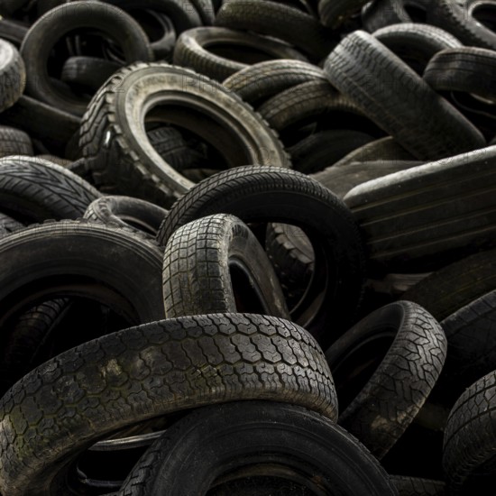 A large collection of worn-out tires is stacked chaotically in a junkyard, illustrating the environmental concerns of tire disposal and recycling efforts. France