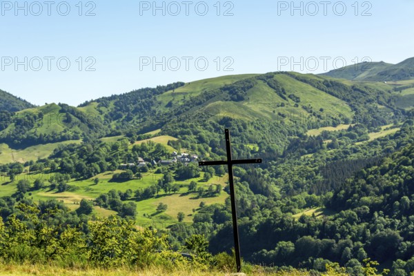 A wooden cross stands prominently against a picturesque landscape of rolling hills and vibrant greenery. The tranquil setting suggests a serene connection with nature, offering breathtaking views. Cezallier. Puy de Dome. Auvergne Rhone Alpes. France