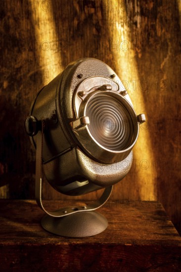 A vintage spotlight rests on a rustic wooden surface, casting a warm glow. Soft light enhances the aged texture of the wood, creating a nostalgic atmosphere