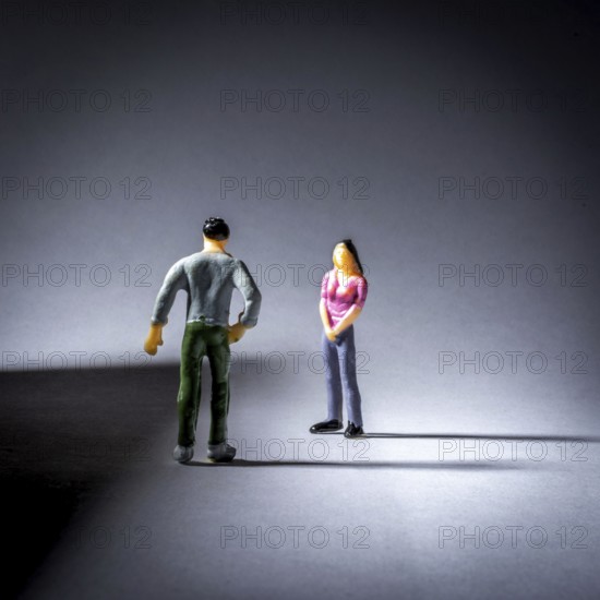 Two small figurines engage in a conversation, with a focus on their body language. The lighting creates a shadow effect, highlighting the interaction