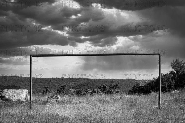 A solitary soccer goal stands in a grassy field under a moody sky filled with dark clouds. Puy de Dome, Auvergne Rhone Alpes, France