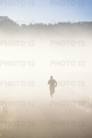 On person training running on a dirt road with morning fog in a rural landscape in autumn