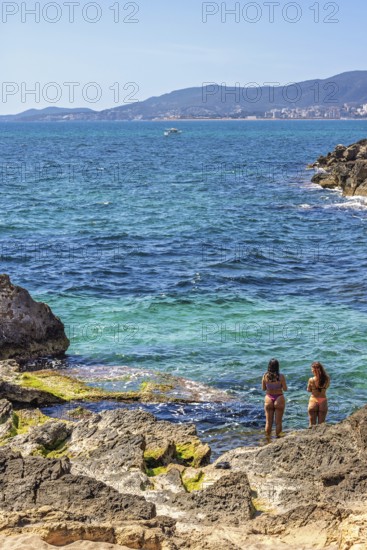 Young women standing in the water by a rocky beach by the sea a sunny summer day, Mallorca, Spain