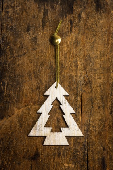 A handcrafted decoration shaped like a fir tree is suspended by a green string against a textured wooden surface. This Christmas ornament adds a festive touch to holiday decor