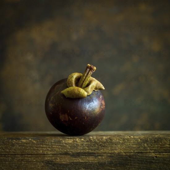 A ripe mangosteen sits gracefully on a weathered wooden surface, showcasing its dark purple skin and crown-like top. The surrounding texture adds depth to the presentation