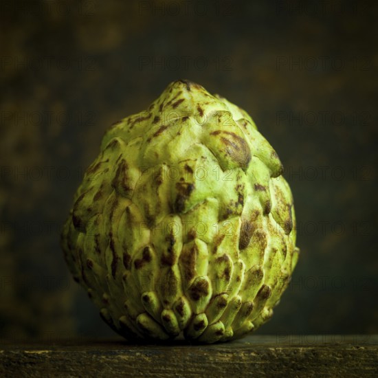 The sugar apple, known as annona squamosa, showcases its unique, scaly green exterior. This exotic fruit is placed on a rustic wooden surface, highlighting its distinct texture and features