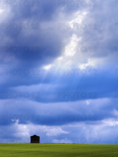 Nestled in a vibrant green field, a solitary hut stands against a backdrop of dynamic clouds, showcasing the natural beauty of Auvergne Rhone Alpes during a clear day. Puy de Dome. Auvergne Rhone Alpes. France