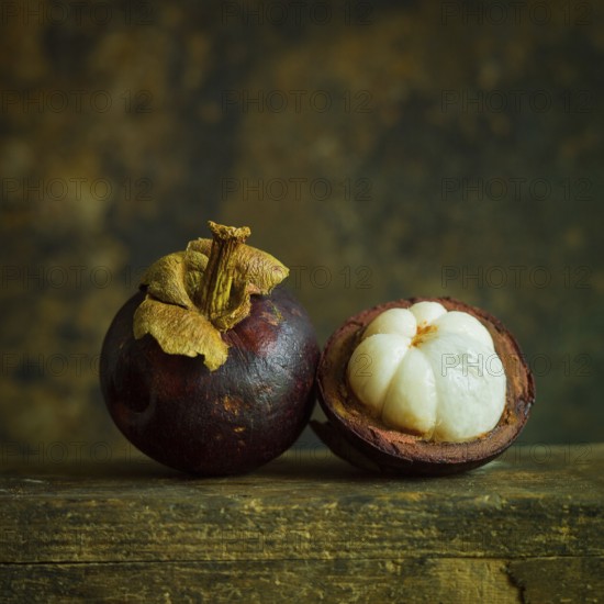 Two ripe mangosteens rest side by side, showcasing their deep purple skin. One fruit is cut in half, revealing the sweet, white segments inside, alluring anyone passing by