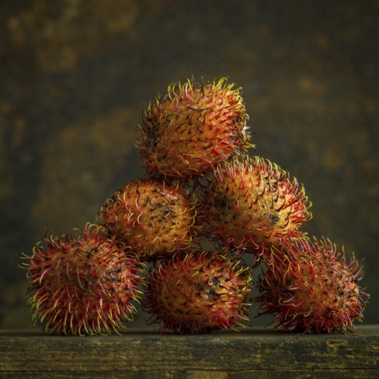 A cluster of rambutans sits on a wooden surface, highlighting their unique hairy skin and rich colors. The soft, warm light enhances the fruit's textured appearance against a rustic backdrop