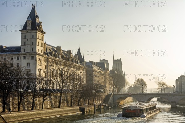 A tour boat navigates the flowing waters of the River Seine, revealing the stunning architecture of Quai des Orfevres and Palais de Justice under a clear sky. Paris. France