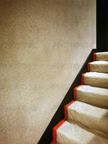 A staircase featuring smooth, soft white steps contrasted by bold orange edges. The surrounding wall is a subtle beige, creating a warm and inviting atmosphere