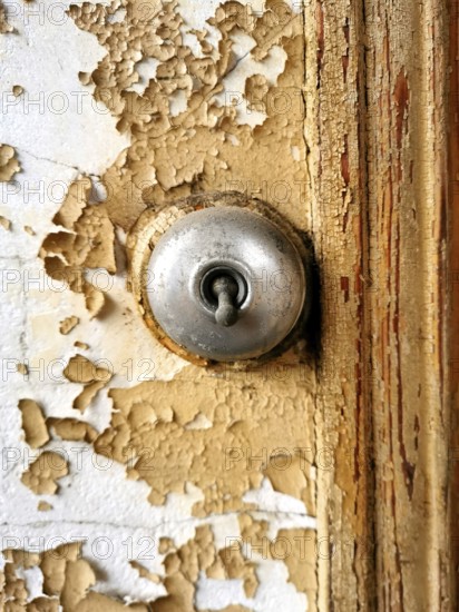 Close view of a keyhole on a weathered, peeling door demonstrates intricate details and textures. The contrast of the metallic keyhole against the aged surface speaks to its history