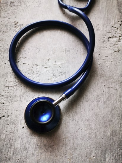 A blue stethoscope lies on a textured surface, its reflection catching the light in a clinical setting. The scene conveys a sense of professionalism and care