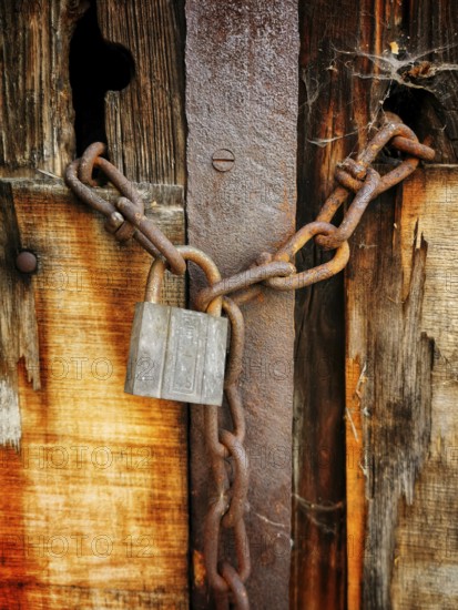 A weathered wooden door displays a rusty padlock and heavy chain, emphasizing neglect and abandonment. The wood shows signs of age, enhancing the overall atmosphere