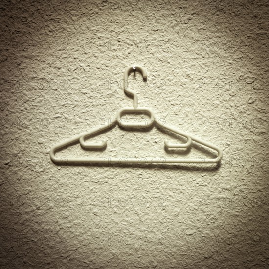 A clothes hanger is displayed prominently against a textured wall, showcasing its sleek design and contributing to a minimalist aesthetic in a casual indoor space. The lighting enhances its features