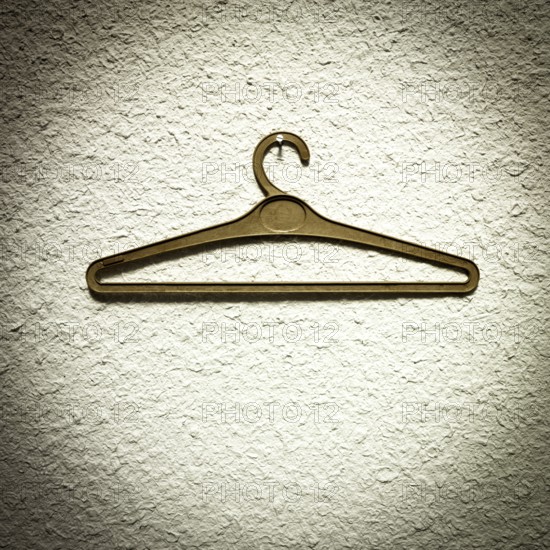 A clothes hanger is suspended from a textured wall, showcasing a minimalist design. The simple indoor setting allows the focus to remain on the hanger, illuminated by natural light