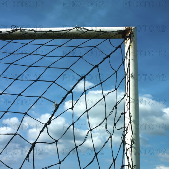 A football goal net is positioned against a cloudy sky, showcasing the intricate details of the netting. The sunlight breaks through, illuminating the scene, hinting at an upcoming match