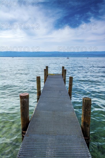 A sturdy jetty extends into the serene waters of Lake Geneva, surrounded by mesmerizing blue hues and a tranquil atmosphere. Perfectly captures the beauty of Haute-Savoie on a peaceful day, Auvergne Rhone Alpes, France