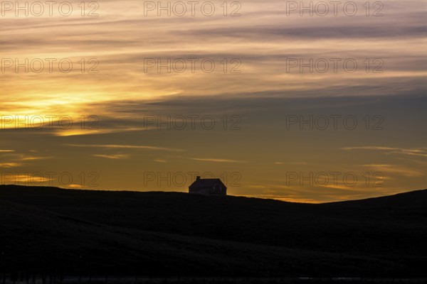 A tranquil farm stands silhouetted against the colorful sky at sunset, showcasing the natural beauty of the Cezallier massif in the Regional Nature Park of Volcans d'Auvergne, Puy de Dome, Auvergne Rhone Alpes, France