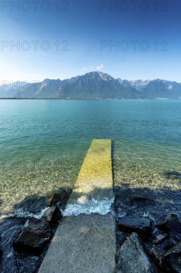 Montreux. A pier stretches out into the tranquil waters of Lake Geneva, surrounded by stunning mountain peaks. Switzerland