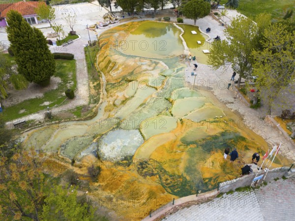 Natural terraces of mineral deposits with people in a green environment, aerial view, Karahayit Kirmizi Su, Red Spring, Pamukkale, Denizli, Turkey