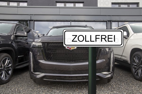 (Photomontage) Symbolic image of the customs agreement between the EU and the USA: sign with the inscription ZOLLFREI in front of a new Cadillac at the dealership