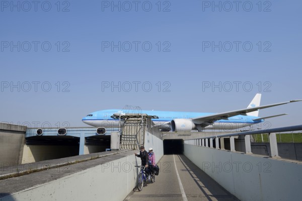 Aeroplane taxiing over a bridge over road and cycle path with cyclists, Amsterdam Airport Schiphol, North Holland, Netherlands