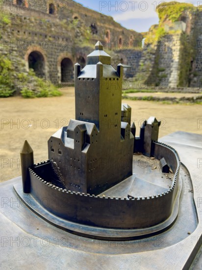 Small metal model of the original fortress building Schloss Burg of the imperial palace of Emperor Frederick I Barbarossa, built in the Middle Ages around 1184 on today's banks of the Rhine, in the background ruins of it, Kaiserswerth, Düsseldorf, North Rhine-Westphalia, Germany