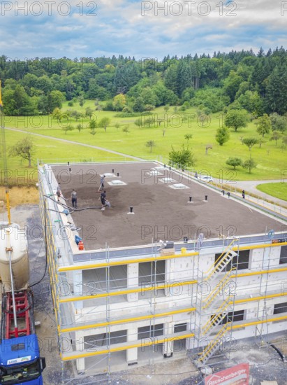Partly completed building with workers in a landscaped environment, surrounded by forest, green roof, house construction, climate neutral