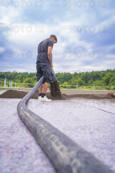 A construction worker distributes materials with a hose on a roof under a cloudy sky, roof greening, house construction, climate neutral