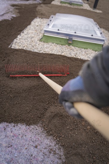 A worker with a rake levels the ground on a roof with gravel beds, roof greening, house construction, climate neutral
